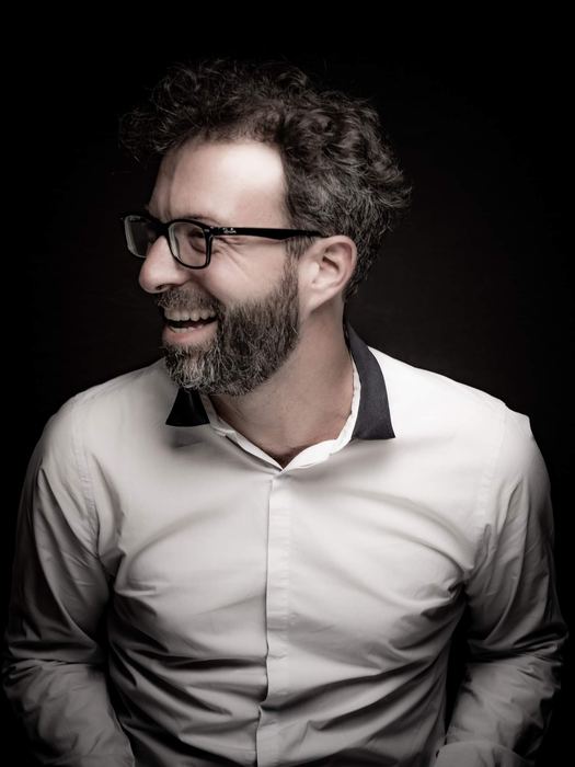 Simon Zaoui riant, de profil, chemise blanche sur fond noir