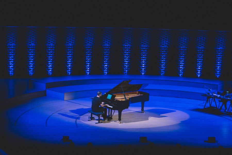 Simon Zaoui au piano à queue dans un halo de lumière, sous un éclairage bleu, à La Seine Musicale