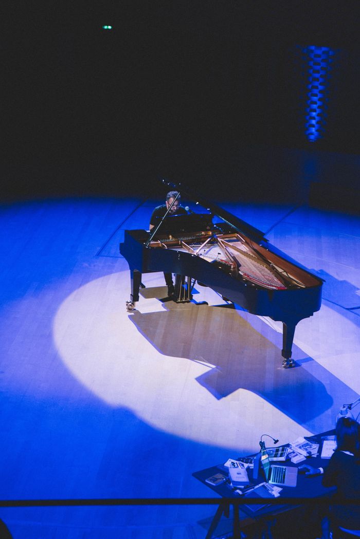 Simon Zaoui au piano à queue, seul dans un cercle de lumière bleue, vu d’en haut