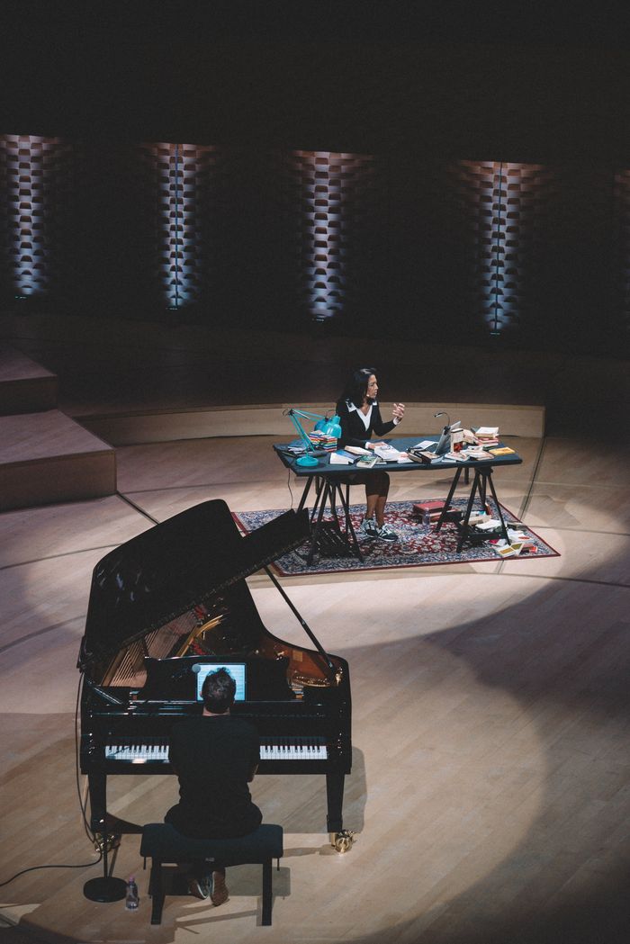 Vue de dessus de la scène : Simon Zaoui au piano au premier plan, Sabine Quindou à son bureau couvert de livres
